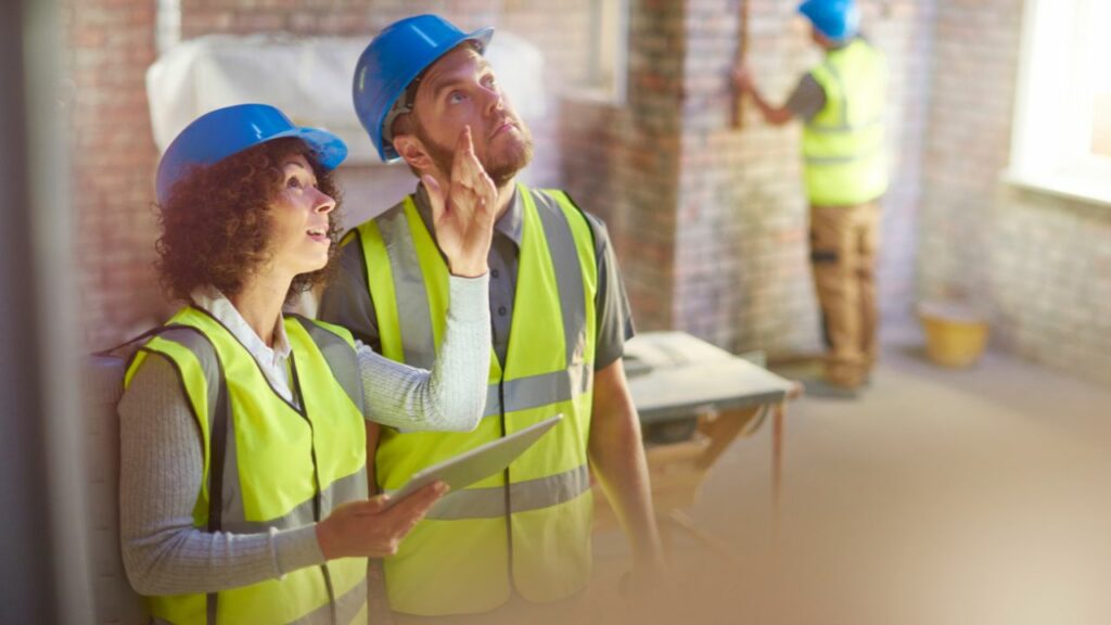 a professional architect is discussing blueprints with a homeowner next to a residential construction site