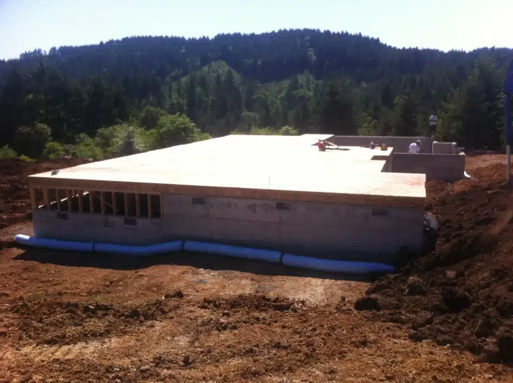Subfloor sheathing installed on a new home foundation with forested hills in the background near Hillsboro, Oregon